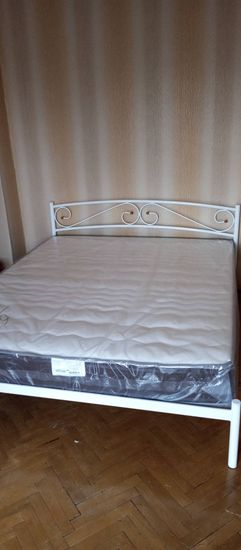 Собрана металлическая рама, установлены ножки, закреплено изголовье, уложен матрас. Все элементы надежно зафиксированы, конструкция устойчива и готова к использованию.