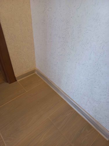 Установлен новый плинтус вдоль стены, аккуратно прилегающий к полу. Все стыки ровные, без зазоров. Цвет гармонирует с покрытием, создавая завершенный вид помещения.