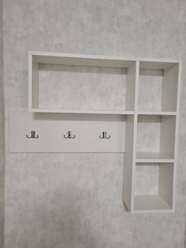 Установлена белая полка с тремя металлическими крючками на светлой стене. Конструкция надежно закреплена, выровнена и готова к использованию.