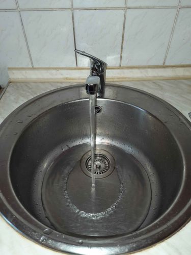 Изображение демонстрирует завершенную работу по замене смесителя на кухонной мойке. Старый кран снят, установлен новый, вода течет плавно, без утечек, поверхность чистая.