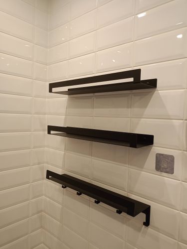 На белой плитке установлены три черные полки, закрепленные на стене. Работа выполнена аккуратно, элементы расположены ровно и надежно.