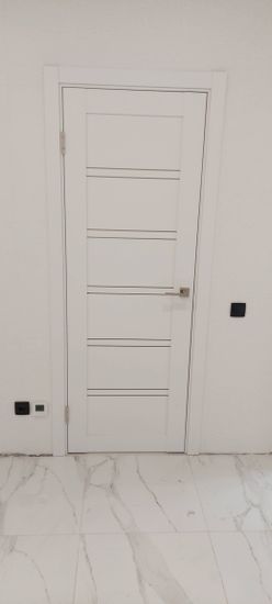 Установлена белая межкомнатная дверь с одной створкой, аккуратно закреплена в проеме, оснащена металлическими петлями и ручкой. Завершено оформление наличников, обеспечена плавная работа.