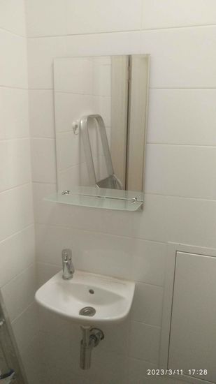 Зеркало аккуратно установлено на стене ванной комнаты, надежно закреплено, дополнено стеклянной полкой, обеспечивая функциональность и эстетичный вид.