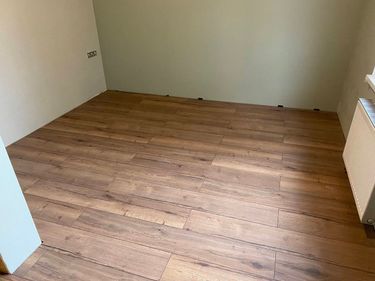 В комнате уложено новое напольное покрытие, демонтаж старого произведен, поверхность выровнена, панели аккуратно состыкованы, зазоры соблюдены, завершено оформление плинтусами.