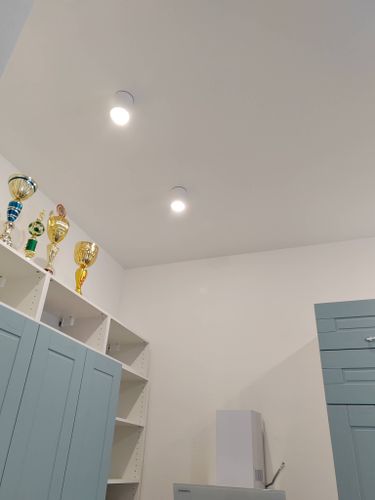 На потолке установлены новые светильники, обеспечивающие равномерное освещение. Провода аккуратно спрятаны, все элементы надежно закреплены, обеспечивая безопасность и эстетичный вид.