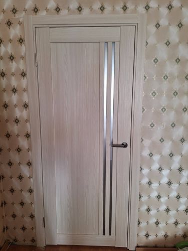 Установлена светлая деревянная дверь с вертикальной вставкой из стекла, закреплена в проеме, добавлены петли, ручка и наличники, обеспечена плавная работа и надежная фиксация.