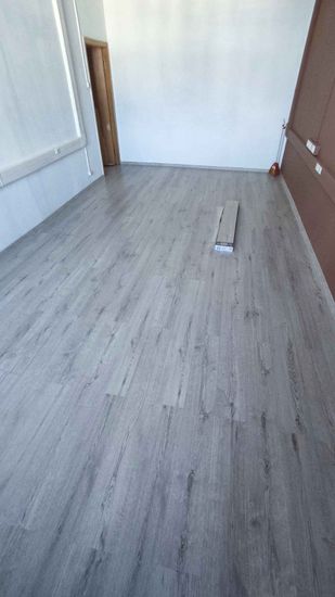 В комнате уложено новое напольное покрытие, серого оттенка, с ровными стыками. Полностью завершена работа по монтажу, обеспечивающая гладкую и эстетичную поверхность.