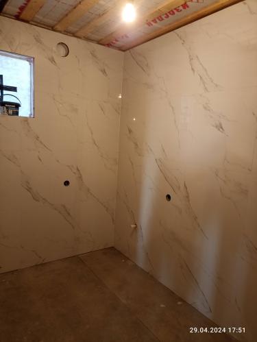 Ванная облицована крупной плиткой с мраморным узором. Стены ровные, швы аккуратные. Установлены отверстия для коммуникаций. Потолок подготовлен, освещение подключено.