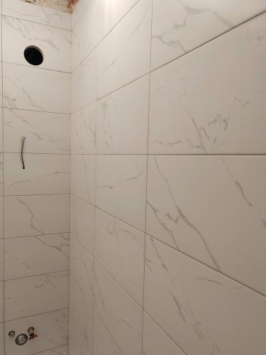 На стене ровно уложены белые плитки с серыми прожилками. Швы аккуратно заделаны, поверхность гладкая и чистая. Видны отверстия для коммуникаций, подготовленные для дальнейшего монтажа.