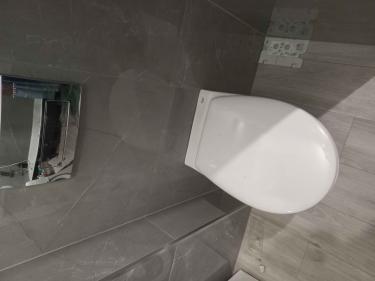 Установлено современное сантехническое оборудование: подвесная чаша закреплена на стене, скрытый бачок интегрирован в конструкцию, подключены коммуникации, выполнена облицовка плиткой.