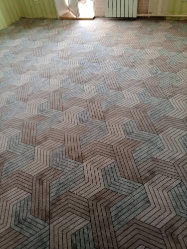 На полу уложены плитки ковра с геометрическим узором, создающим гармоничный и аккуратный вид. Все элементы ровно подогнаны, образуя единое покрытие без зазоров.