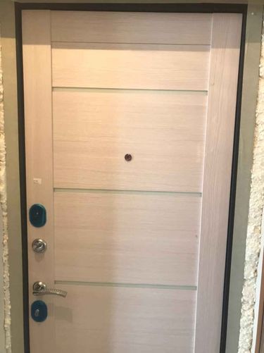 Дверь покрыта МДФ панелями, установлены новые замки и ручка, добавлен глазок. Поверхность гладкая, светлая, с горизонтальными линиями. Завершено оформление и монтаж.