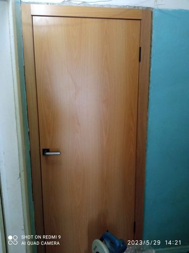 На деревянной двери установлено запирающее устройство. Выполнены точные вырезы, закреплены ручка и механизм. Конструкция функционирует исправно, обеспечивая надежность и удобство.