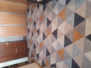 На полу уложено покрытие с геометрическим узором, тщательно подогнанное по краям, без складок и неровностей. Цветовая гамма гармонично сочетается с интерьером комнаты.