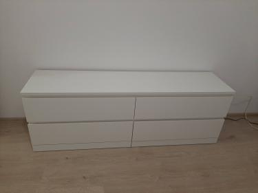 Собран белый комод с четырьмя ящиками. Все детали соединены, ящики установлены, конструкция устойчива. Комод стоит на полу, готов к использованию.