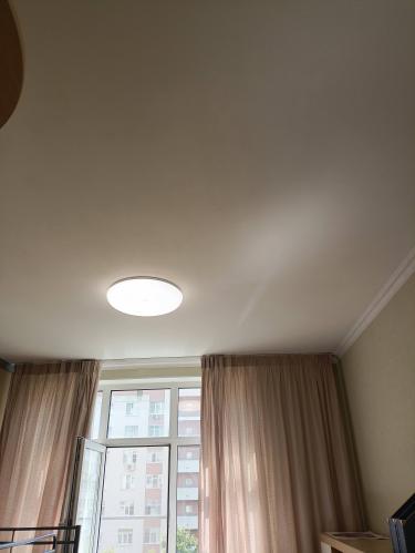 Выполнен монтаж светильника на потолке, подключение к электросети, проверка работоспособности, закрепление на поверхности. Устройство функционирует, освещая пространство комнаты.