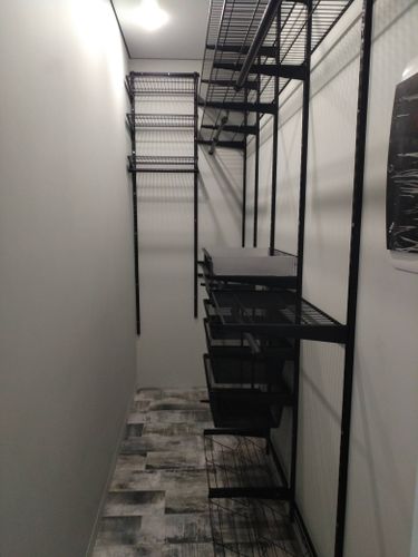 Установлен металлический турник в узком помещении, закреплён на стене. Стойки и перекладины надежно зафиксированы, обеспечивая устойчивость и безопасность использования.