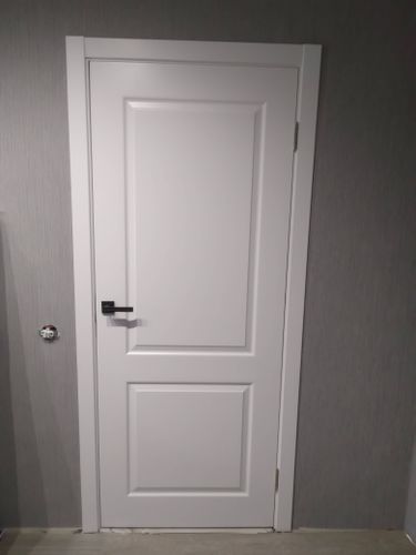 Установлена белая дверь с ручкой и петлями, выполнена подгонка коробки, закреплены наличники, проверена плавность открывания и закрывания, обеспечена надежная фиксация в проеме.
