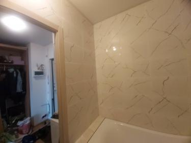 На стенах ванной комнаты уложена керамическая плитка с мраморным узором. Швы аккуратно затерты, поверхность ровная и гладкая, создавая эстетичный и завершенный вид.