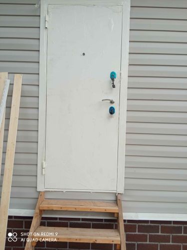 Установлена новая металлическая дверь с замками и ручкой, закреплена в проеме, обеспечена надежная фиксация, проверена функциональность, завершены отделочные работы вокруг конструкции.