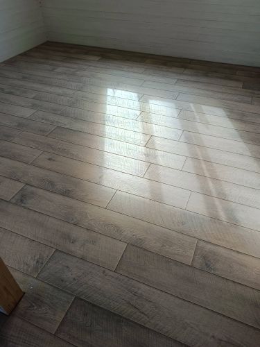 На ровную поверхность уложено напольное покрытие, доски плотно соединены, образуя гладкую текстуру. Завершён монтаж, обеспечивающий эстетичный вид и долговечность пола.