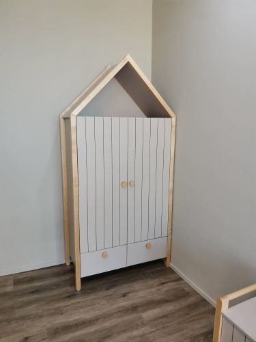 Собран шкаф в форме домика, установлены дверцы и ручки, закреплены боковые панели, выровнены детали, обеспечена устойчивость конструкции, завершена установка в углу комнаты.