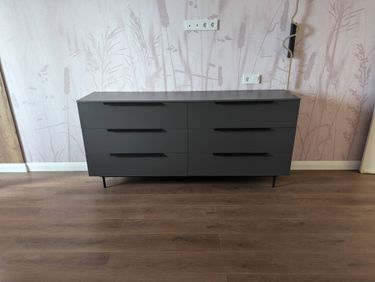 Собран новый комод с шестью ящиками, установлен на ровный пол, выровнен по уровню, закреплены ручки, проверена плавность выдвижения ящиков, устойчивость конструкции обеспечена.