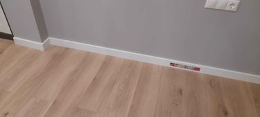 Установлен новый плинтус вдоль стены, аккуратно закреплённый по периметру комнаты. Завершённые работы обеспечивают эстетичный переход между полом и стеной, создавая завершённый вид интерьера.