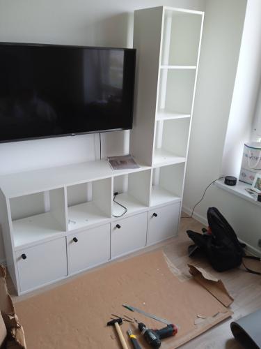 Собран белый шкаф с полками и дверцами, установлены ручки. Все элементы закреплены, конструкция устойчива. Вся работа выполнена аккуратно, инструменты убраны.