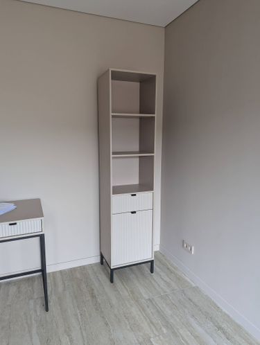 Собран высокий шкаф с полками и ящиком, установлен в углу комнаты, выровнен по уровню, закреплены все детали, проверена устойчивость конструкции, завершена сборка.