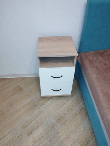 Собрана прикроватная тумба: установлены ящики, прикреплены ручки, закреплены боковые панели и верхняя крышка. Все детали надежно соединены, обеспечивая устойчивость и функциональность.