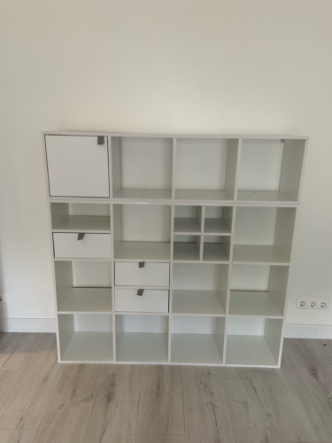 Собран белый шкаф с полками и ящиками, установлены дверцы и ручки, обеспечена устойчивость конструкции, проверена функциональность всех элементов.