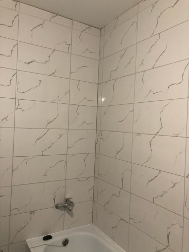 На стенах ванной комнаты уложена керамическая плитка с мраморным узором. Швы аккуратно заполнены затиркой, поверхность ровная и гладкая, создавая современный и стильный вид.