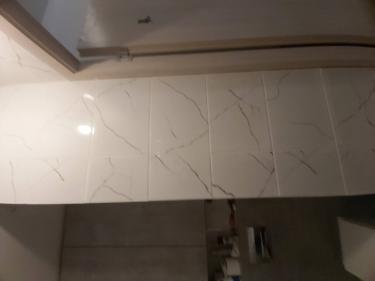 Плитка аккуратно уложена на стену, швы ровные, поверхность гладкая. Завершенный процесс создает эстетичный вид, обеспечивая долговечность и прочность покрытия.