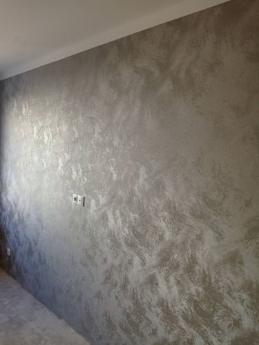 На стену нанесены декоративные обои с текстурой, создающей эффект мрамора. Поверхность ровная, без видимых швов и пузырей, что придаёт помещению стильный и современный вид.