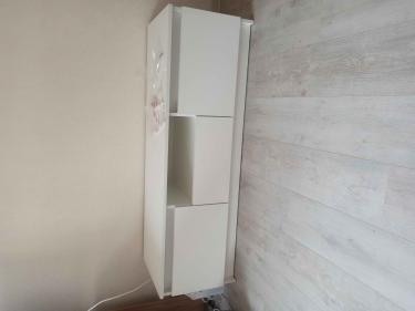 Собрана белая тумба: установлены дверцы, закреплены полки, выровнена конструкция, прикручены ножки, проверена устойчивость, убраны лишние детали. Готова к использованию.