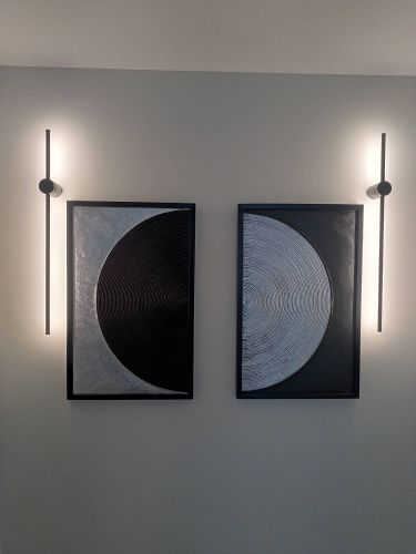 Изображение демонстрирует два абстрактных полотна, закрепленных на стене. Они симметрично расположены между светильниками, создавая гармоничный акцент в интерьере.