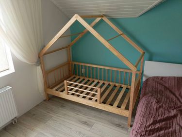 Собрана деревянная кровать с каркасом в форме домика. Установлены боковые панели, закреплены рейки основания. Конструкция устойчива и готова к эксплуатации.