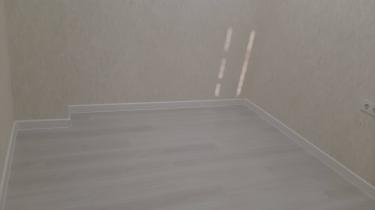 В комнате уложено напольное покрытие, ровно и аккуратно, с установленными плинтусами вдоль стен. Цвет покрытия светлый, создающий ощущение простора и чистоты.