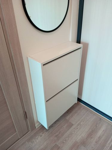 Круглое зеркало аккуратно закреплено на стене, обеспечивая надежность и эстетичный вид. Под ним расположен белый шкаф, создающий гармоничный интерьер.