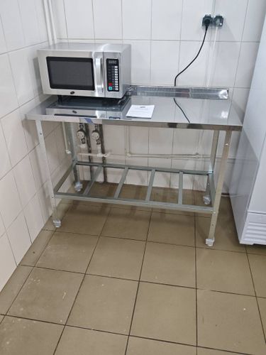 Собрана металлическая конструкция с полкой, на которой размещена микроволновая печь. Стеллаж установлен на плиточный пол, подключены розетки для электроприборов.