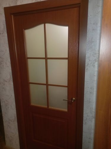 Установлена новая деревянная дверь с матовым стеклом, закреплена в проеме, проверена работа замка и ручки, отрегулированы петли для плавного открывания, завершена отделка наличниками.