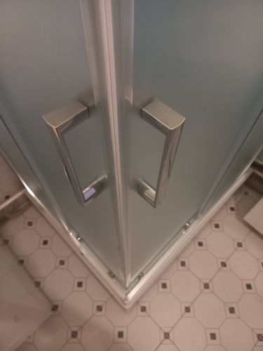 Установлена новая душевая кабина с прозрачными дверями и металлическими ручками на месте прежней ванны. Поддон закреплён на плиточном полу, обеспечивая современный вид и функциональность.