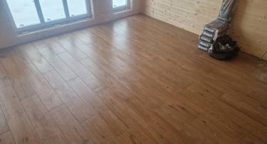 На ровное основание уложена плитка, имитирующая дерево. Поверхность получилась гладкой и ровной, швы аккуратно заделаны, создавая цельный и эстетичный вид.