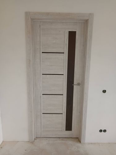 Установлена светлая межкомнатная дверь с вертикальным стеклянным элементом, закреплена в проеме, добавлены наличники, врезана ручка, обеспечена плавная работа конструкции.