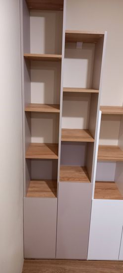 Собран аккуратный стеллаж из деревянных панелей, установлены полки, закреплены элементы. Конструкция устойчива, готова к использованию, подходит для хранения предметов.