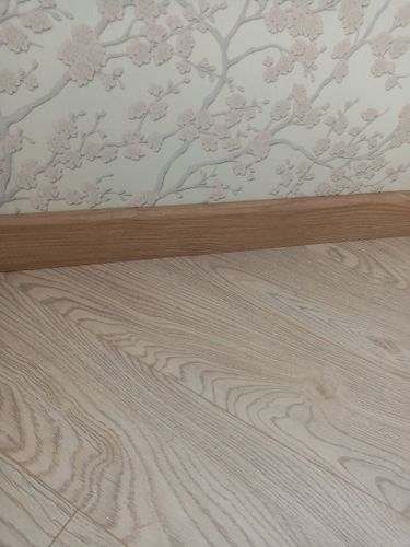 Установлен скрытый плинтус, аккуратно примыкающий к стене с цветочным узором. Плинтус гармонично сочетается с текстурой пола, создавая единый стиль интерьера.