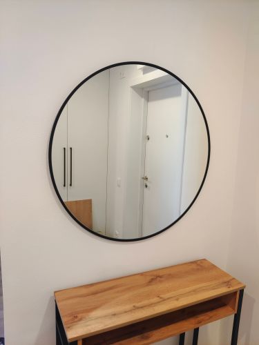 Круглое зеркало аккуратно закреплено на стене, выровнено по уровню, надежно зафиксировано, гармонично вписывается в интерьер, создавая уют и визуально расширяя пространство.