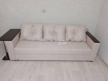 Собран диван: установлены подлокотники, закреплены спинка и сиденье, прикручены ножки, добавлены подушки. Готов к использованию, стоит на светлом полу у стены.