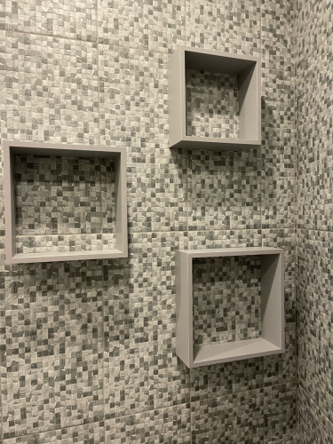 На стене закреплены три серых квадратных полки, расположенных в шахматном порядке. Фон выполнен из плитки с мозаичным узором.